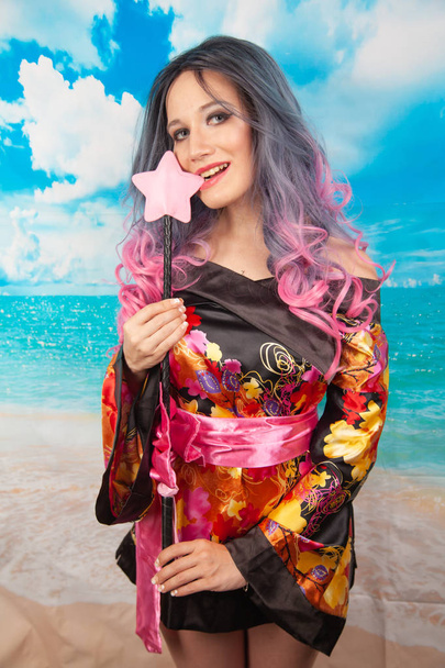 una encantadora joven con el pelo Ombre se encuentra en una túnica de kimono y sostiene una estrella de cuero en sus manos
 - Foto, Imagen