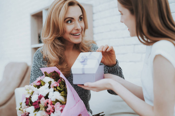Smiling Daughter Gives Mother Flowers and Gift. Relationship in Family. Holiday at Home. Happy Mother. Friendly Relations. Celebrating Together. Happiness in Family Concept. Presenting Gift. - Фото, зображення