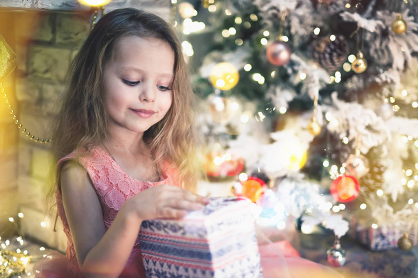 Happy child girl unpacks her present on Christmas night. - Photo, image