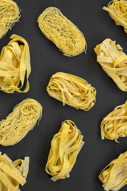 Set of various uncooked pasta(fettuccine, pappardelle, tagliolini) on black background, overhead view. Flat lay, from above, top view. - Photo, Image