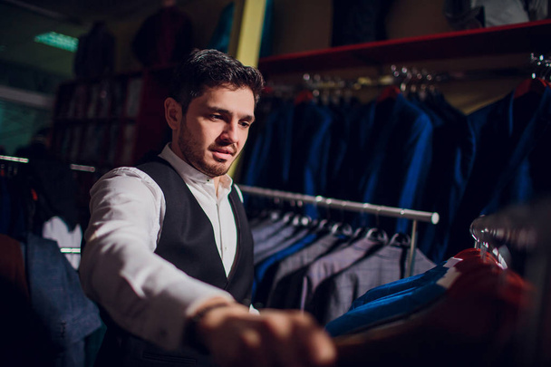 Tailor, tailoring. Mens suit, tailor in his workshop. Elegant mans suits hanging in row. Luxury mens classic suits on rack in elegant mens boutique. - Φωτογραφία, εικόνα