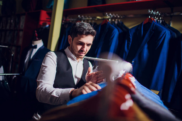 Tailor, tailoring. Mens suit, tailor in his workshop. Elegant mans suits hanging in row. Luxury mens classic suits on rack in elegant mens boutique. - Photo, Image