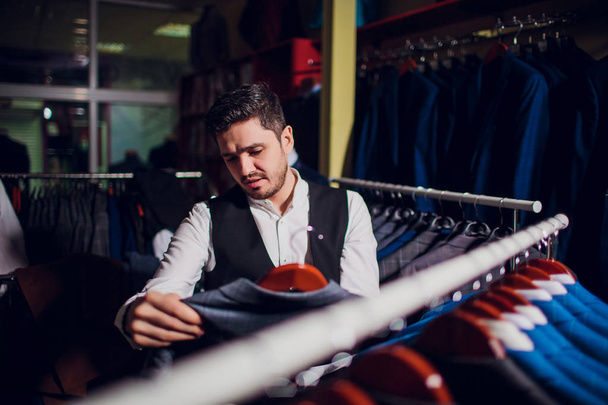 Tailor, tailoring. Mens suit, tailor in his workshop. Elegant mans suits hanging in row. Luxury mens classic suits on rack in elegant mens boutique. - Фото, изображение