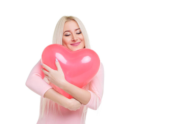 Beautiful young blond woman with heart shape pink air balloon on white isolated background. Woman on Valentine's Day. Symbol of love - Image - Fotoğraf, Görsel