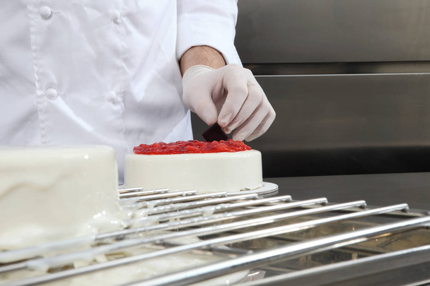 main pâtissier prépare un gâteau, couvrir de glaçage et décorer avec des fraises, travaille sur un plan de travail de cuisine industrielle en acier inoxydable
 - Photo, image