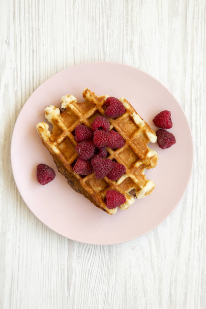 Traditional belgian waffle with raspberries on pink plate on white wooden background, top view. Flat lay, overhead, from above. Closeup. - Photo, Image