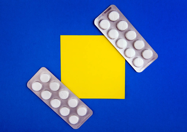 Pills and Empty Yellow Paper on the Blue Cardboard Background - Foto, afbeelding