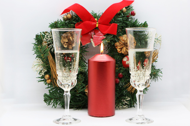 Deux verres de champagne, une bougie rouge allumée, une couronne sur fond blanc
. - Photo, image