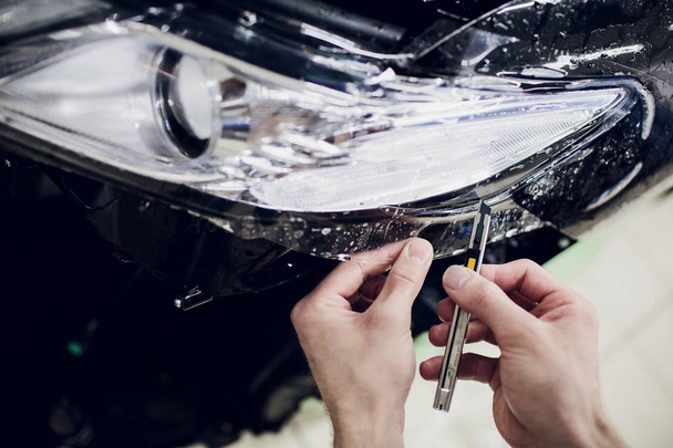 Worker hands installs car paint protection film wrap auto headlight - Foto, Imagen