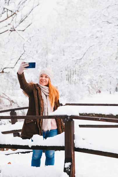 Νεαρή γυναίκα παίρνει μια selfie σε ένα πάρκο μια χιονώδη χειμερινή ημέρα - Φωτογραφία, εικόνα