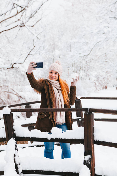 Νεαρή γυναίκα παίρνει μια selfie σε ένα πάρκο μια χιονώδη χειμερινή ημέρα - Φωτογραφία, εικόνα