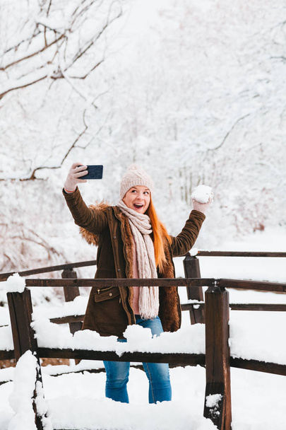 Young woman taking a selfie in a park on a snowy winter day - Photo, Image