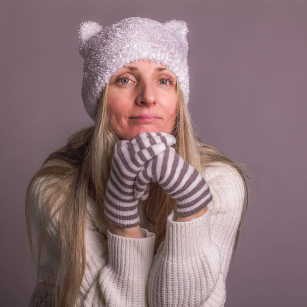 Imagen de la señora pensativa vestida con ropa de invierno, suéter blanco, sombrero con orejas y guantes a rayas, buscando calma, posando, plano de estudio
. - Foto, imagen