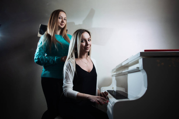 Two young beautiful girls playing the piano. Girls learn to play a musical instrument. - Foto, afbeelding