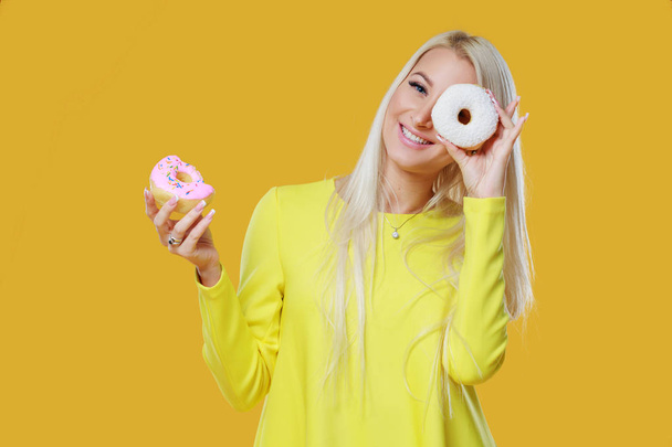 Woman Choosing between two donuts with sprinkles on a yellow background. Concept of food and Tasty - Zdjęcie, obraz