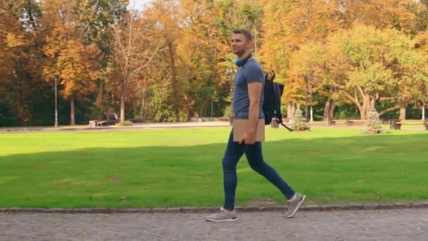 щасливий студент з рюкзаком тримає ноутбуки та книжкову ходьбу в міському парку. красивий осінній пейзаж
 - Кадри, відео
