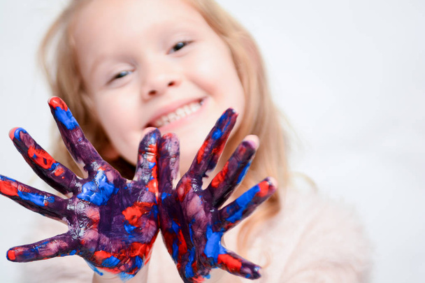 Onnellinen lapsi leikkii maalilla, tytöllä on maali käsissä ja sormissa
 - Valokuva, kuva