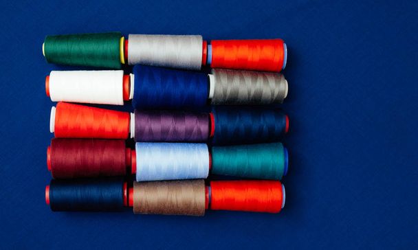 Zestaw nici w różnych kolorach na niebieski backgtound. Wiele wątków do szycia i haftu różnią się w kolor i rozmiar. Wielokolorowe palety wątków. - Zdjęcie, obraz