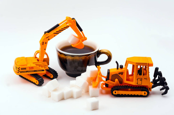 máquinas de construcción de juguetes carga azúcar en una verdadera taza de café sobre un fondo claro
 - Foto, Imagen