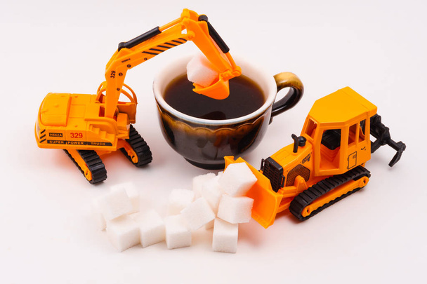 toy construction machines loads sugar into a real cup of coffee on a light background - Photo, Image