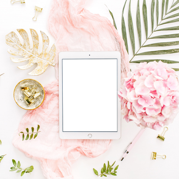 Blank screen tablet, pink hydrangea flowers bouquet, tropical palm leaf, pastel blanket, monstera leaf plate and accessories on white background. Flat lay, top view rose gold home office desk workspace mockup. - Photo, Image