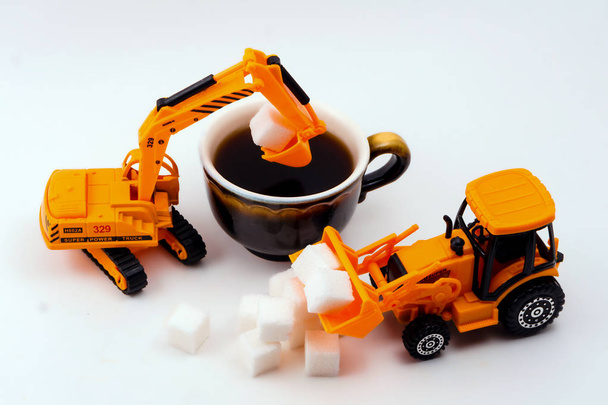 игрушечные строительные машины загружает сахар в реальную чашку кофе на легком фоне
 - Фото, изображение
