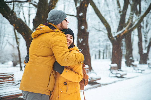 ζευγάρι αγκαλιά στο πάρκο χιονισμένου χειμώνα. πίνοντας τον καφέ να πάμε να ζεσταθεί σε κρύα ημέρα έννοια - Φωτογραφία, εικόνα