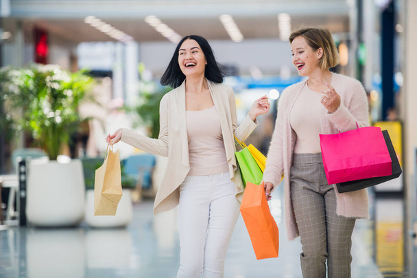 Laughing girls carrying bags with purchases in shopping mall - Photo, Image