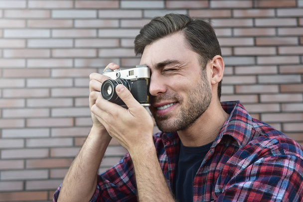Man with retro photo camera Fashion Travel Lifestyle outdoor while standing against brick wall background. - Photo, Image