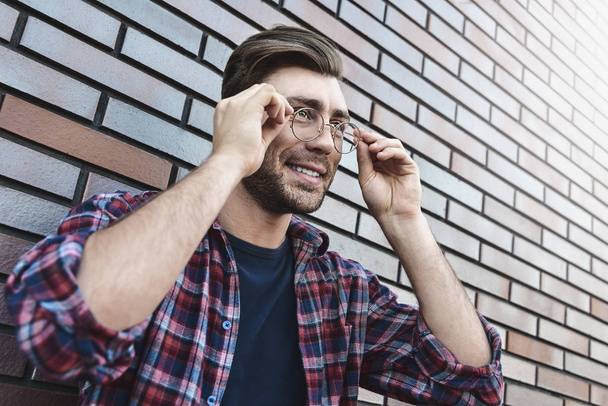Ať se usmívám pohledný muž v kulaté brýle a tričko izolované na hnědá cihlová zeď - Fotografie, Obrázek