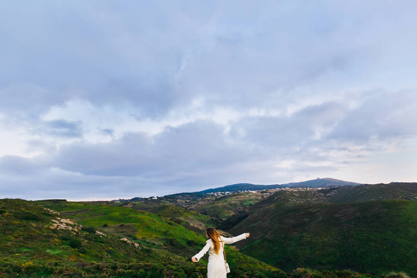 το κορίτσι με μοντέρνα ρούχα που τρέχει πάνω στους λόφους και κρατά τα χέρια της στις πλευρές - Φωτογραφία, εικόνα