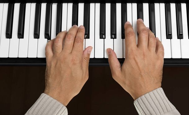 Вид зверху рук, що грають на клавіатурі фортепіано акорд А
 - Фото, зображення
