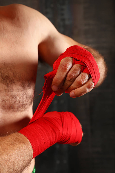 Close up man boxer wrapping red hand wraps over wrists preparing for fight, over black background with copy space, low angle view - Foto, immagini