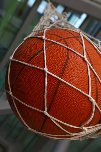 Close up one basketball ball hanging in mesh sack, low angle side view - Photo, Image