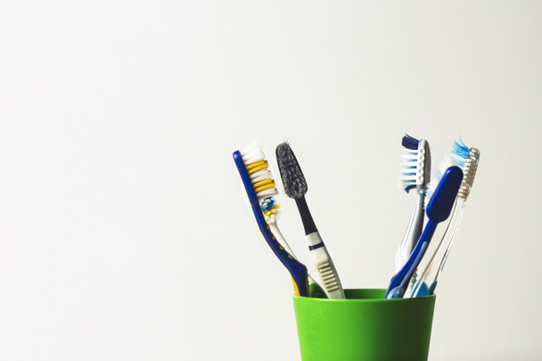 Beaucoup de brosses à dents dans une tasse en plastique sur fond blanc. Le concept de changer de brosse à dents, hygiène buccodentaire, dentisterie, une famille nombreuse et conviviale
 - Photo, image