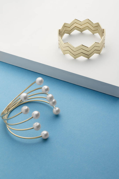 Bracelet en forme de zigzag doré sur surface blanche et bracelet doré avec perles sur bleu divisé
 - Photo, image