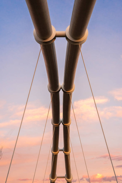 Symmetrical steel pipes supporting a suspension bridge over a river. - Photo, Image