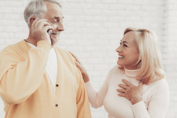 Smiling Old Man and Woman Talking on Smartphone. Sitting on White Sofa. Smiling Woman. Grandfather and Grandmother. Family at Home. Using Digital Gadget. Holding Cell Phone. Talking on Phone. - Foto, imagen