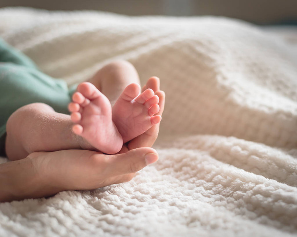 Close-up little pink toes of newborn Asian baby in his mom hands with cozy blanket background. Love, family and protection concept - Photo, Image
