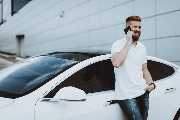 Man Talks On Phone Near Tesla Car. Charge Station. Automobile Parking Lot. Innovation Technology. New Generation Electro Hybrid Vehicle. Ecology Station. Futuristic Power. Gadget Concept. - Fotografie, Obrázek