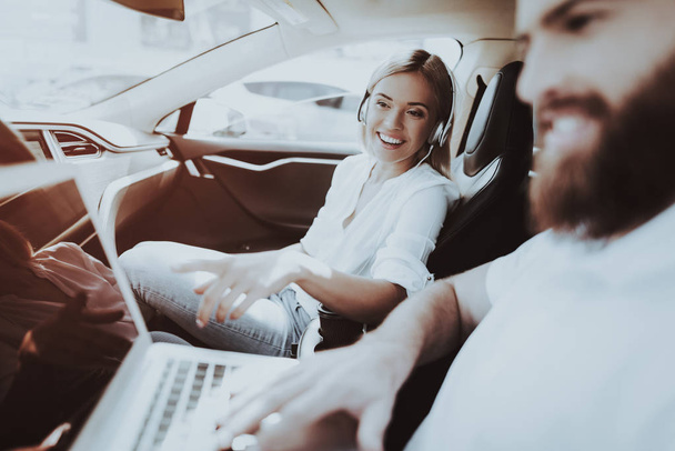 Man Works With Laptop. Girl In Headphones. Tesla Car. Front Seat. Innovation Technology. New Generation Electro Hybrid Vehicle. Luxury Design. Futuristic Power. Resring Together. Test Driving. - Zdjęcie, obraz