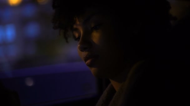 African-american woman sitting in automobile, looking on smartphone, nighttime - Felvétel, videó