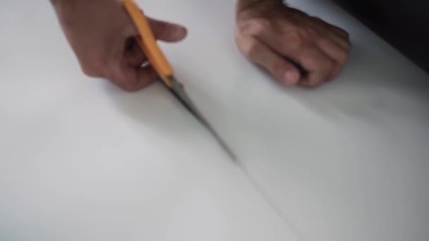 Camera shows male workers hands cutting white sheet with orange scissors. - Footage, Video