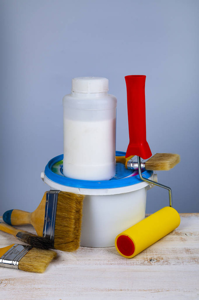 Paint can, roller and brush on the table. Items for home or office renovation on gray background. - Photo, Image