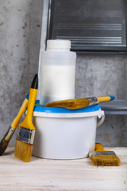 Paint can and brush on the table. Items for home or office renovation against a gray wall and ladder. - Photo, Image
