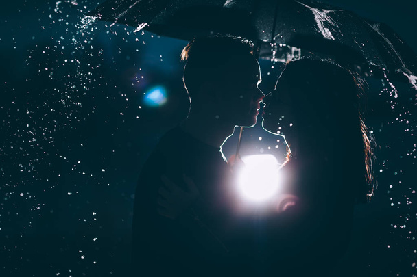 young couple standing under a dark umbrella. - Foto, afbeelding