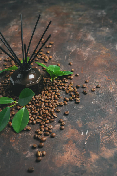 Aroma reed diffuser with rattan sticks, green leaves and coffee beans on dark surface - 写真・画像