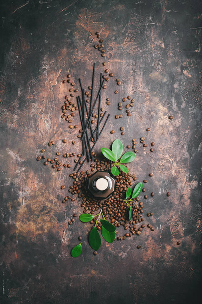 Top view of aroma reed diffuser with rattan sticks, green leaves and coffee beans on dark surface - Fotoğraf, Görsel