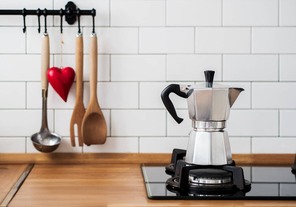 Silver Moka coffee pot on gas stove against wall with white tiles in kitchen  - Foto, afbeelding
