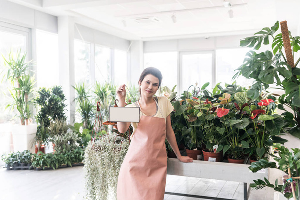 young female florist holding blank banner with empty space for text in greenhouse - Foto, imagen